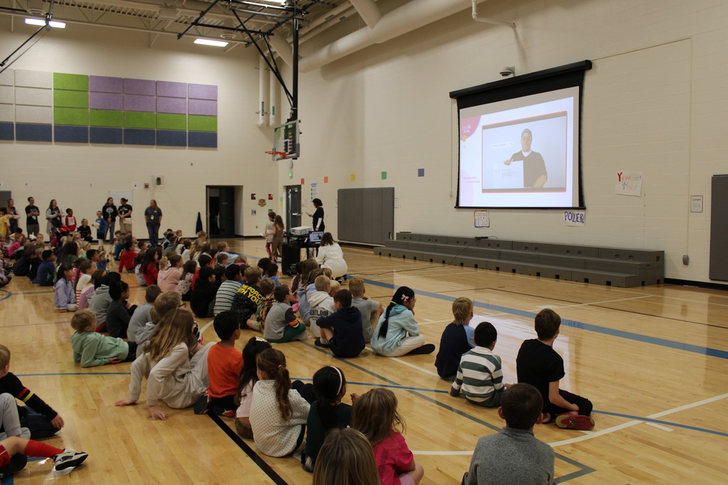 Students sit in rows in the gym watching a video about responsibility.