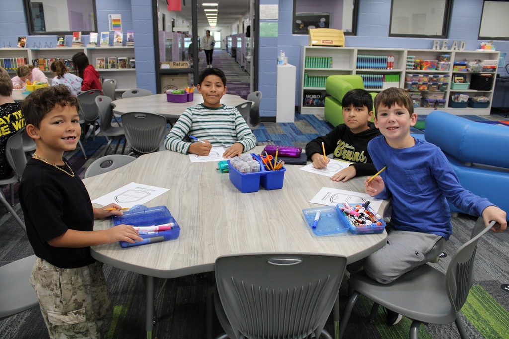 Two first grade boys and two fifth grade boys sit at a table working on a responsibility shield.