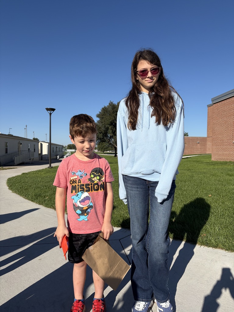 A boy in a red "On A Mission" t-shirt standing beside an older girl wearing a light blue hoodie and sunglasses.