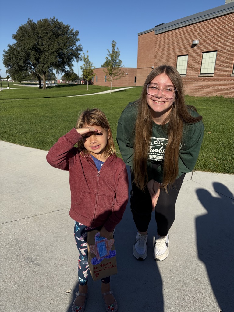 A younger child in a maroon jacket shading her eyes, standing beside an older girl wearing a dark green sweatshirt leaning forward.