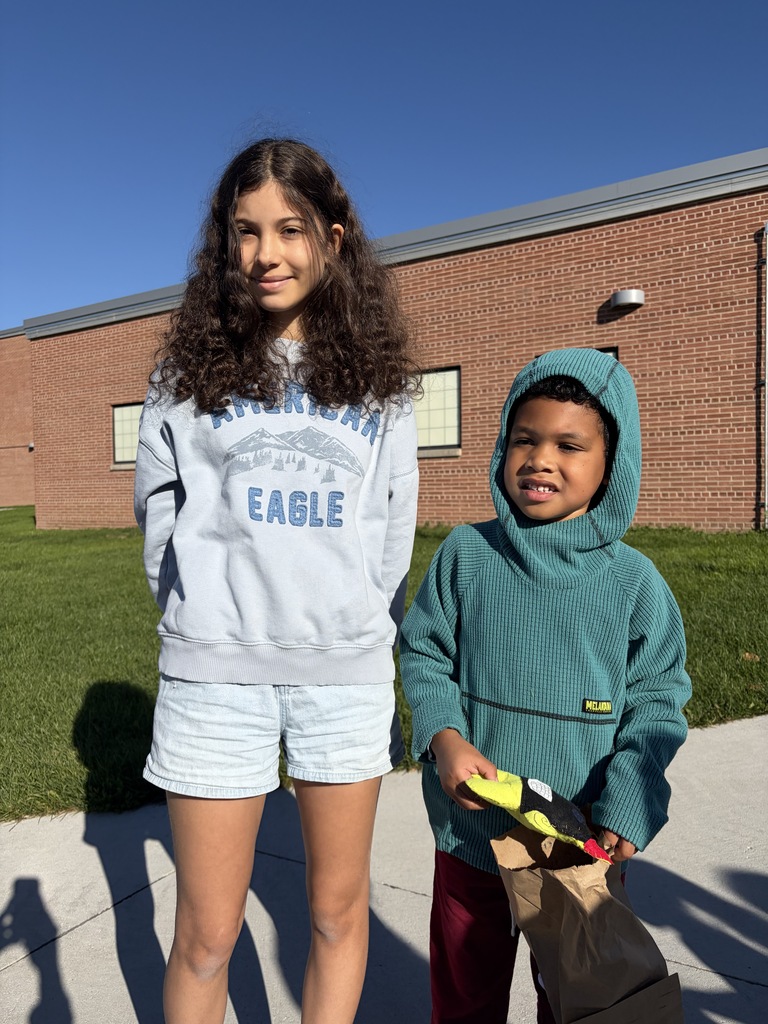 A girl in a light blue "American Eagle" sweatshirt paired with a younger boy wearing a green hooded sweater holding a small craft item and paper bag.