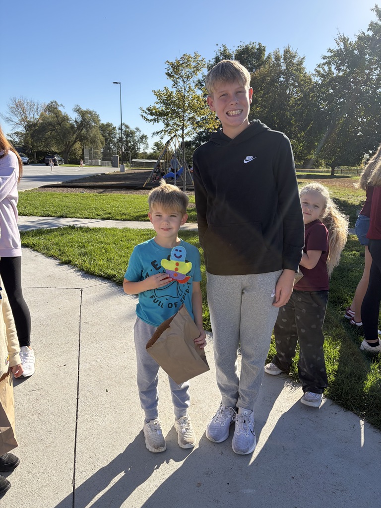 A boy holding a colorful gingerbread cutout and brown paper bag, standing with a tall boy in a dark Nike hoodie.