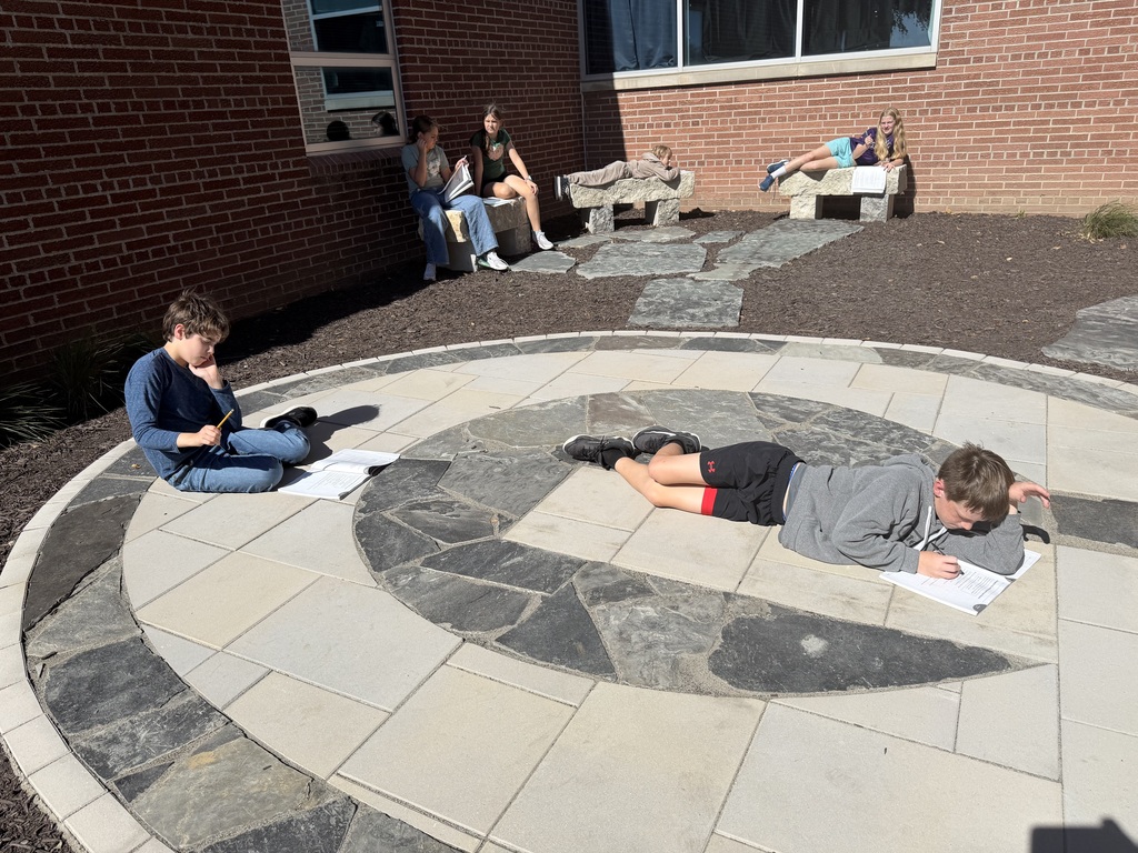 Students studying and reading outdoors while sitting and lying on stone pavers and benches in a courtyard setting.
