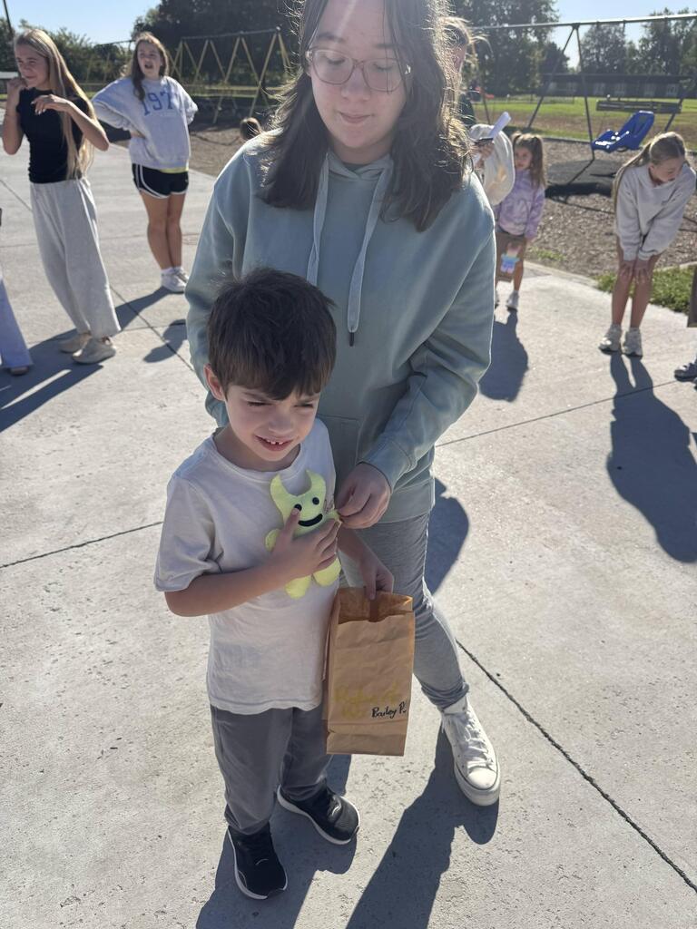 Older student standing behind a young boy holding a yellow plush toy and a decorated paper bag.
