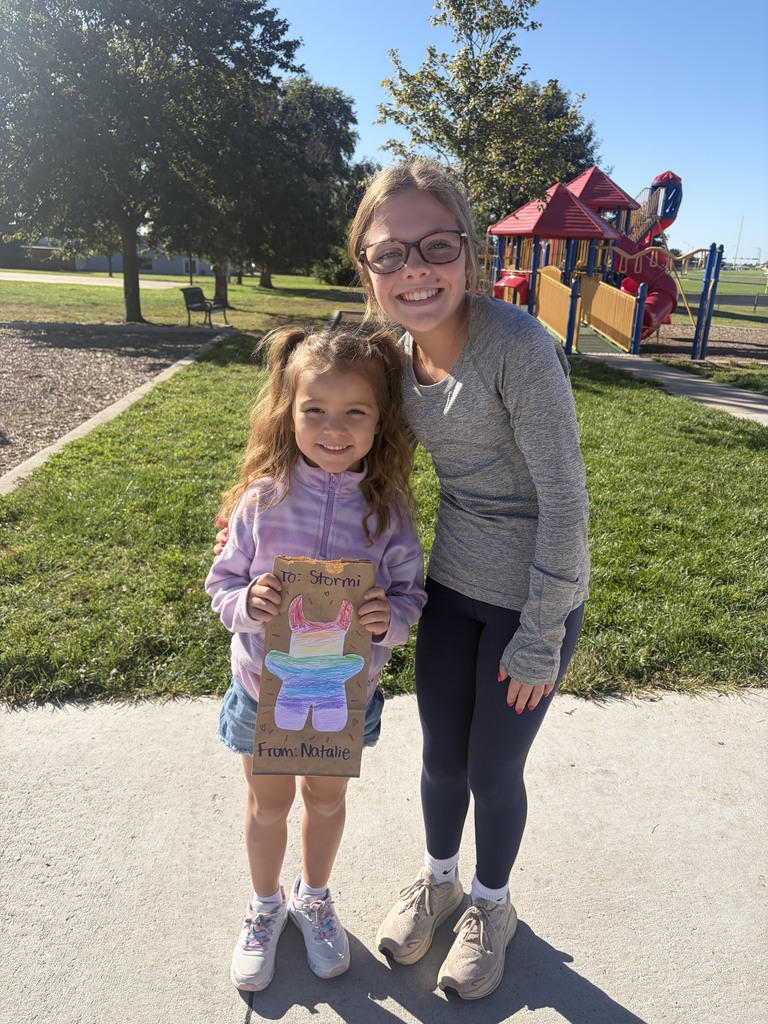 Older student smiling next to a young girl holding a decorated paper bag with a colorful monster drawing.