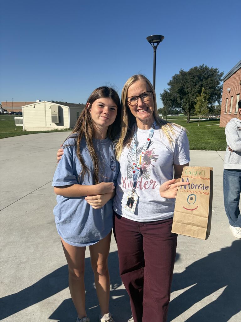 Teacher and student posing together outdoors while holding a paper bag labeled "Calvin's Monster".