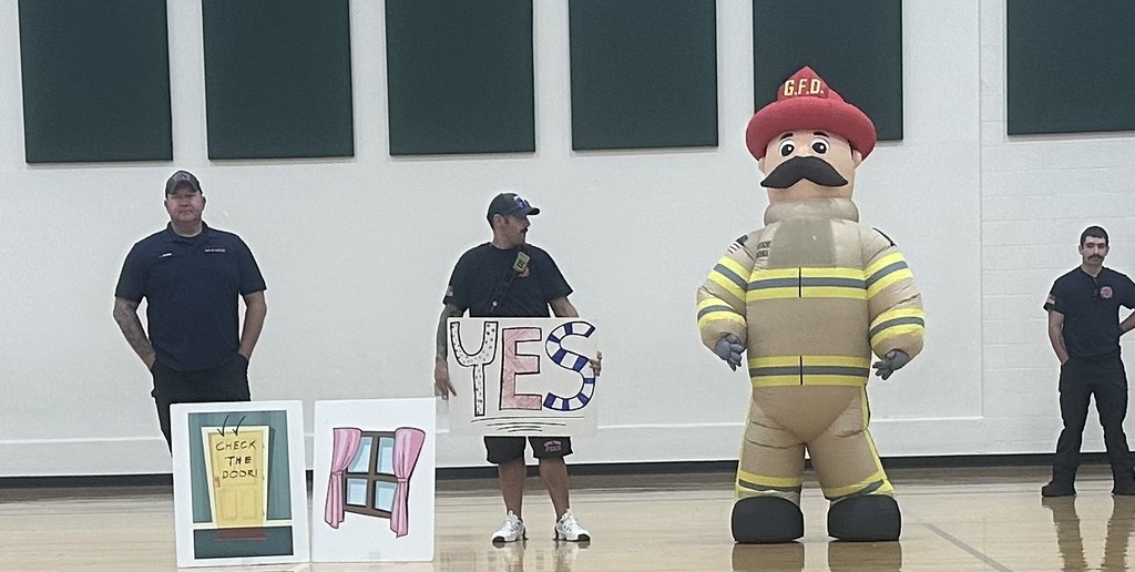 Firefighters and the mascot training students in the gym. 
