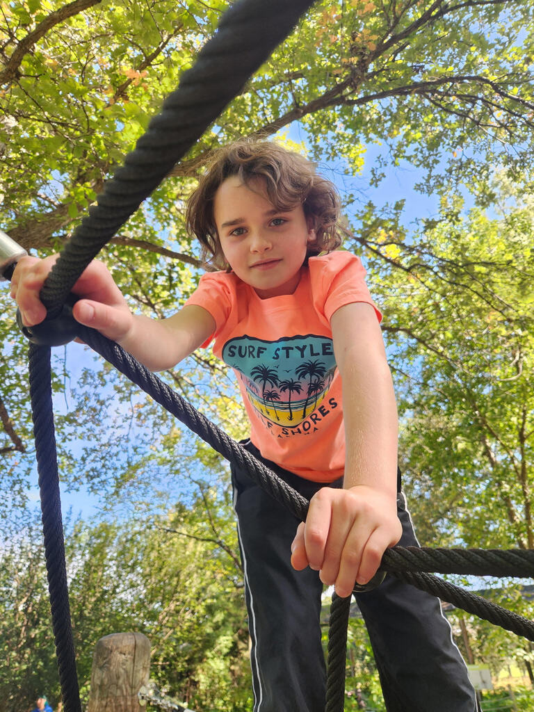 Boy wearing an orange shirts holds on to a spider web rope