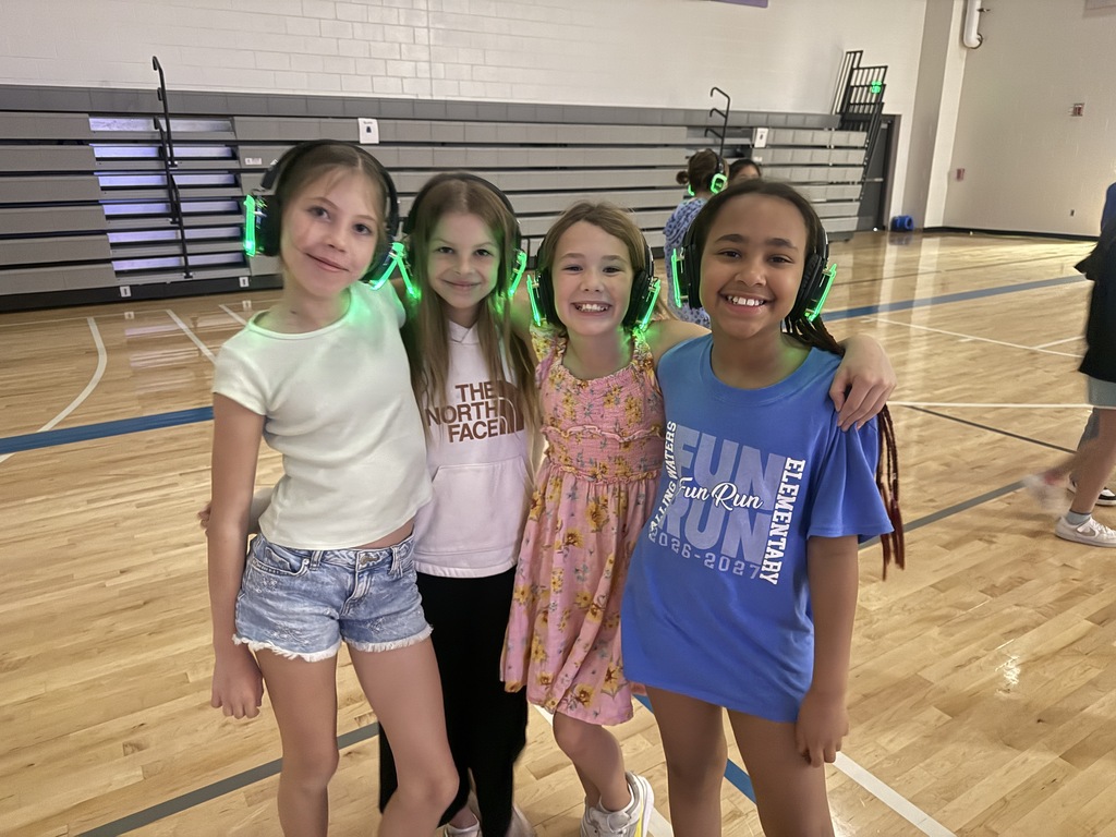 four 4th grade girls stand in a group with their silent disco headphones