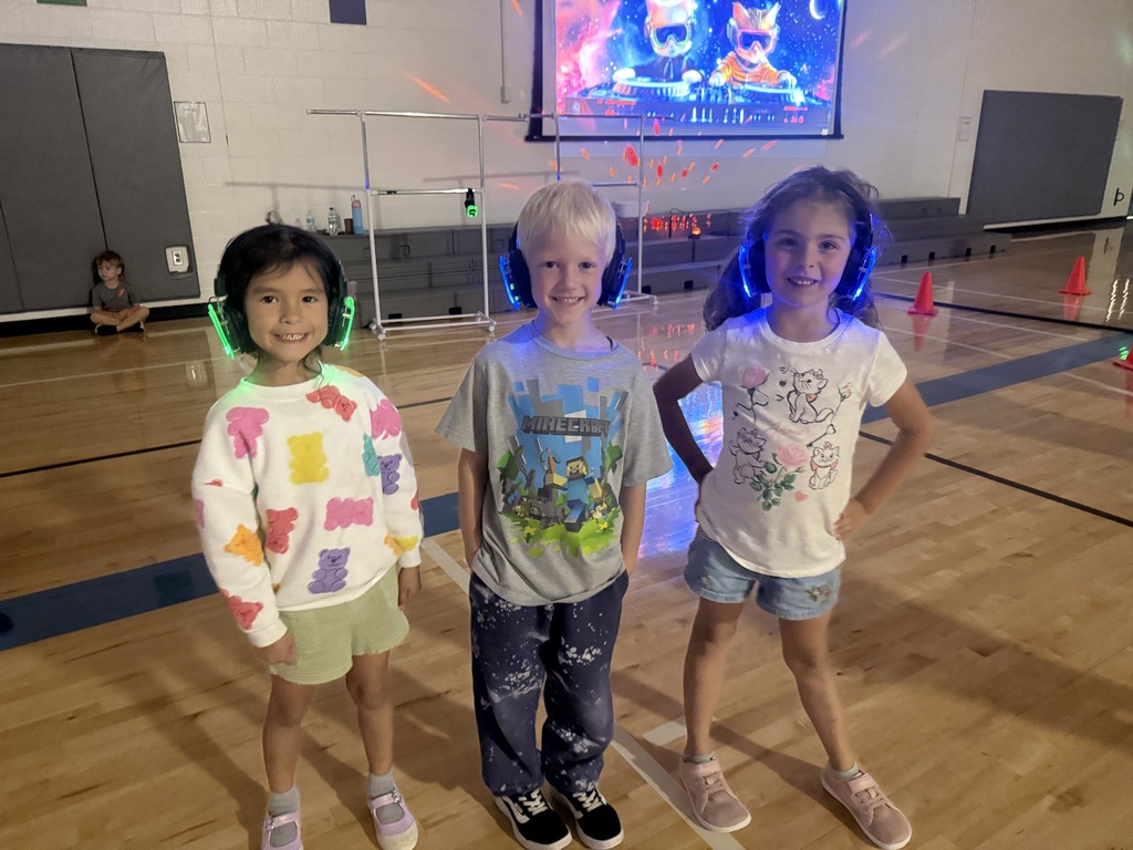 2 kindergarten girls and 1 boy stand with their silent disco headphones.