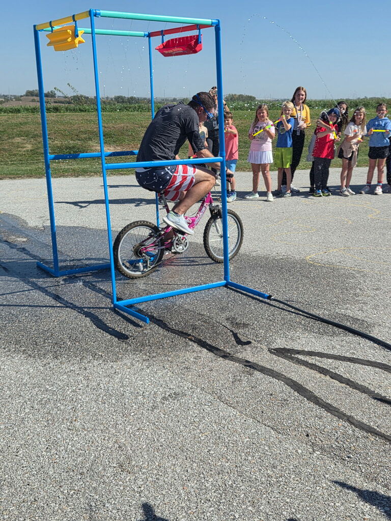 Mr. Basye rides bike through the PTO carwash and kids soak with water