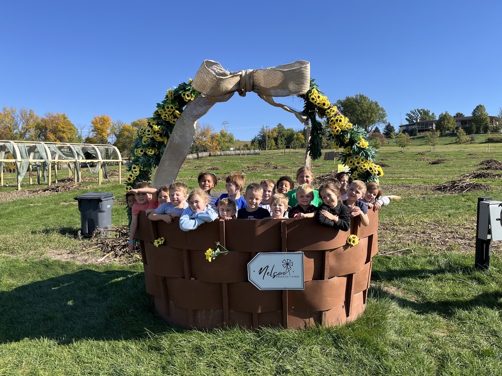 Large group of young students smiling together inside a giant decorative woven basket adorned with sunflowers and a burlap bow.