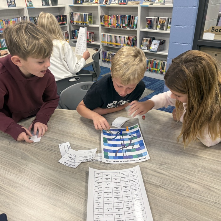 two third grade boys and one girl are playing a board game at a table