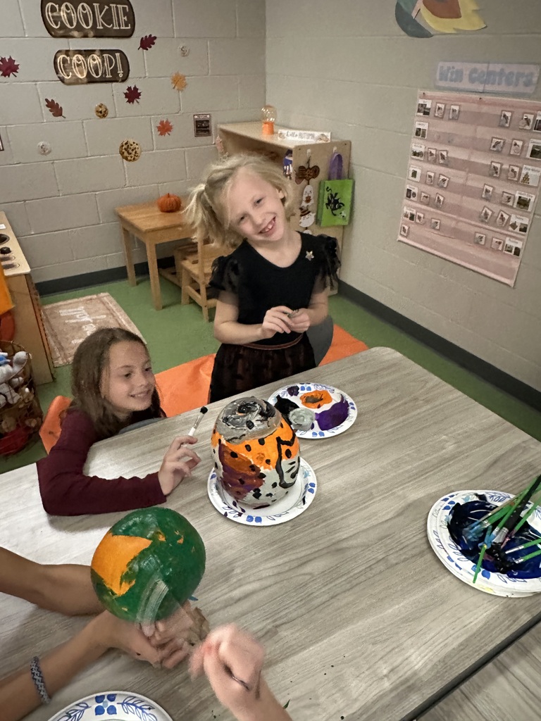 students painting a pumpkin at a table in a classroom