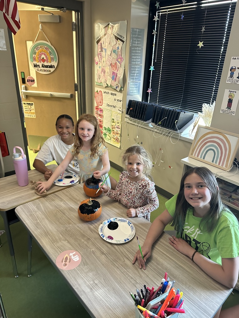 students paint pumpkins together in a classroom at a long table