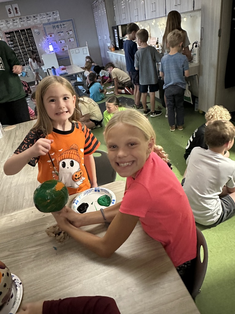 two students smiling at the camera painting a pumpkin