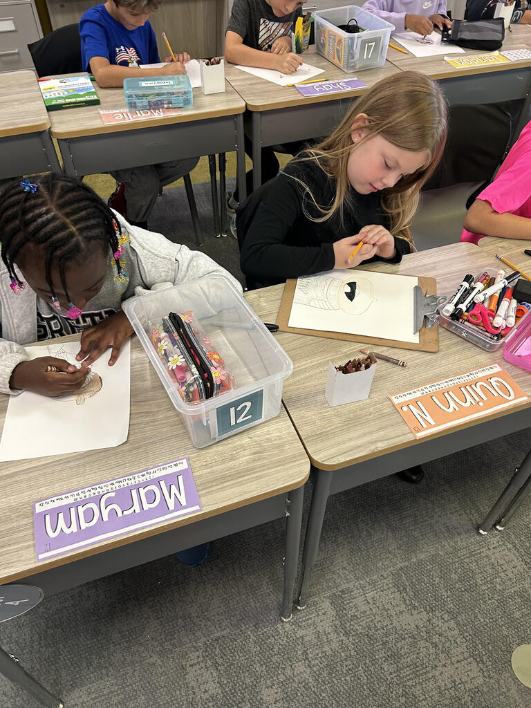 Students at their desk working on a buddy art project in a classroom.