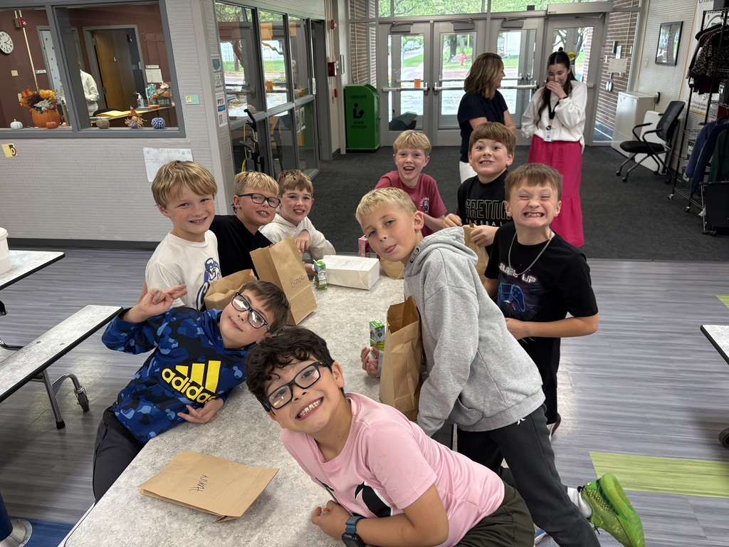 Group of elementary school boys leaning together around a cafeteria table, making playful faces and smiling for a group picture.