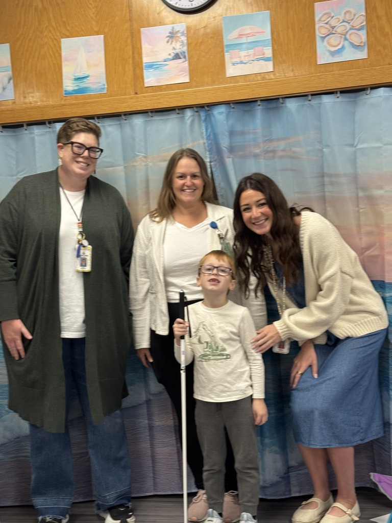 A young boy holding a white cane poses with three smiling women standing behind him against a beach curtain backdrop.
