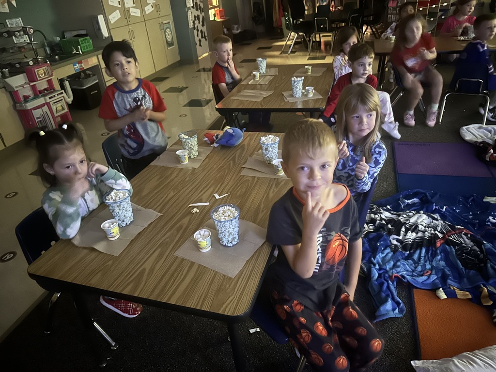 More students are eating popcorn, marshmallows, and M&Ms at tables.