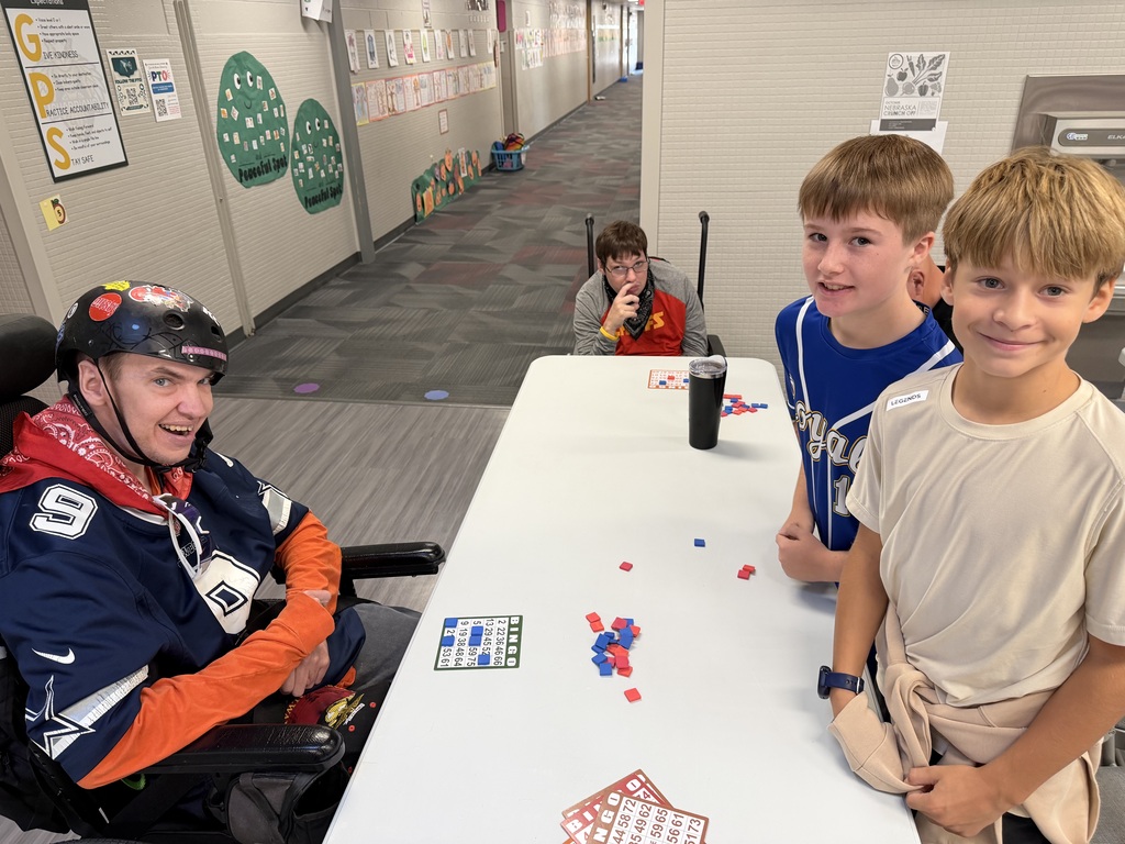 Group of participants gathered around a table playing bingo in a school hallway, with two young boys smiling for the photo.