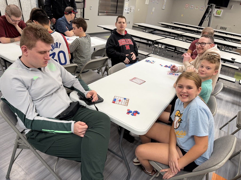 Participants gathered at a white table in a school cafeteria, smiling together during a bingo game activity.