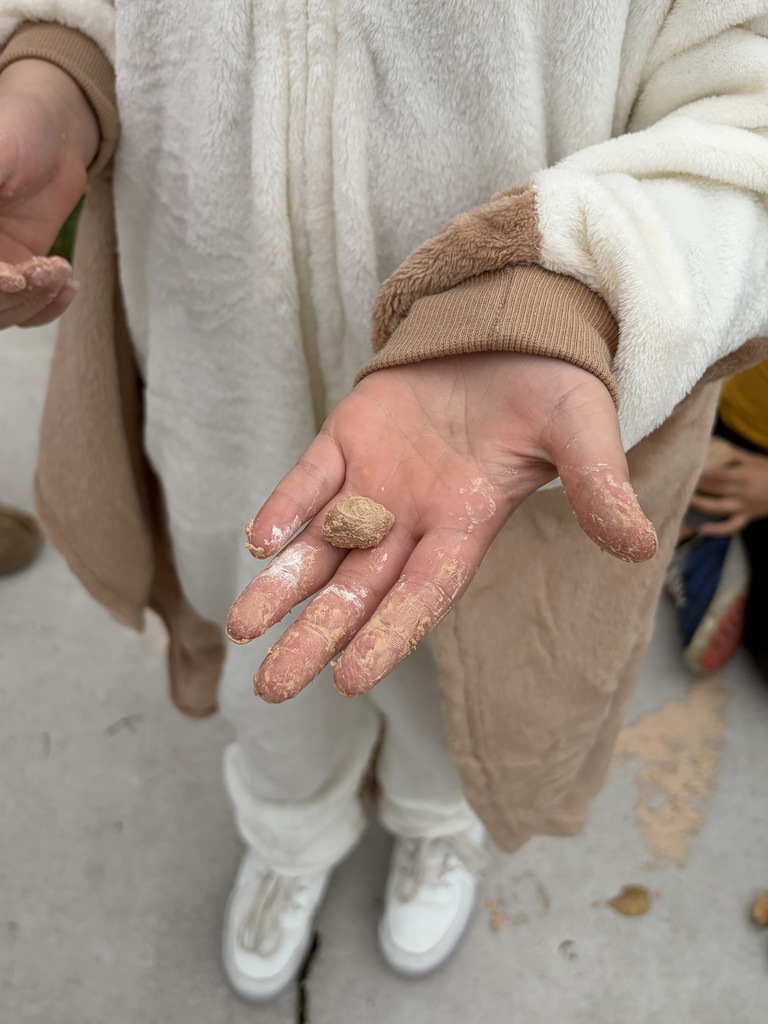 Detailed close-up of a student's dust-covered hands holding a small fossil uncovered during a classroom outdoor activity.