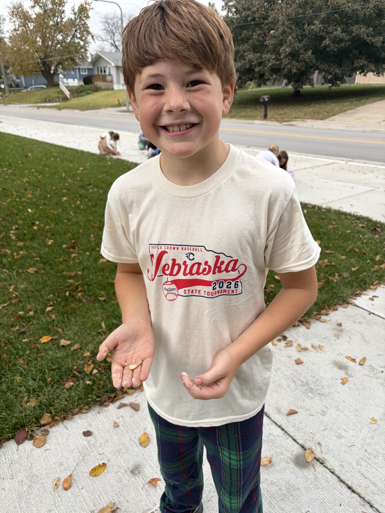 Young boy wearing a Nebraska t-shirt smiling outdoors while showing dusty hands from a fossil digging activity.