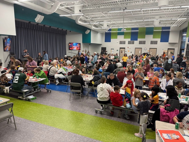 Families seated in the commons area of the elementary school. Students are wearing costumes and families are playing bingo.