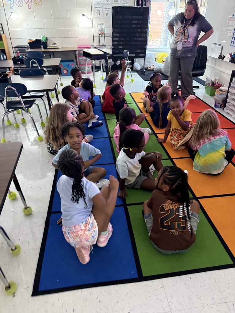 students on carpet facing each other, in pairs, answering a question to their partner
