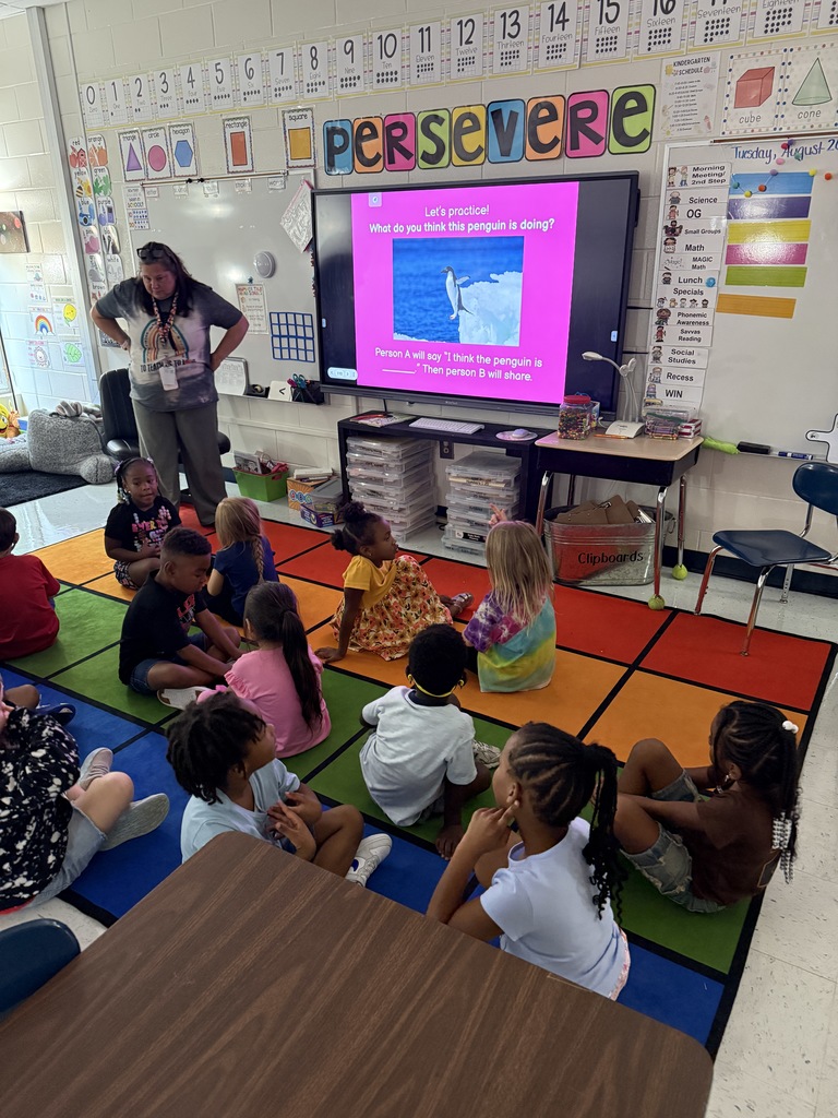students on carpet facing each other, in pairs, answering a question to their partner