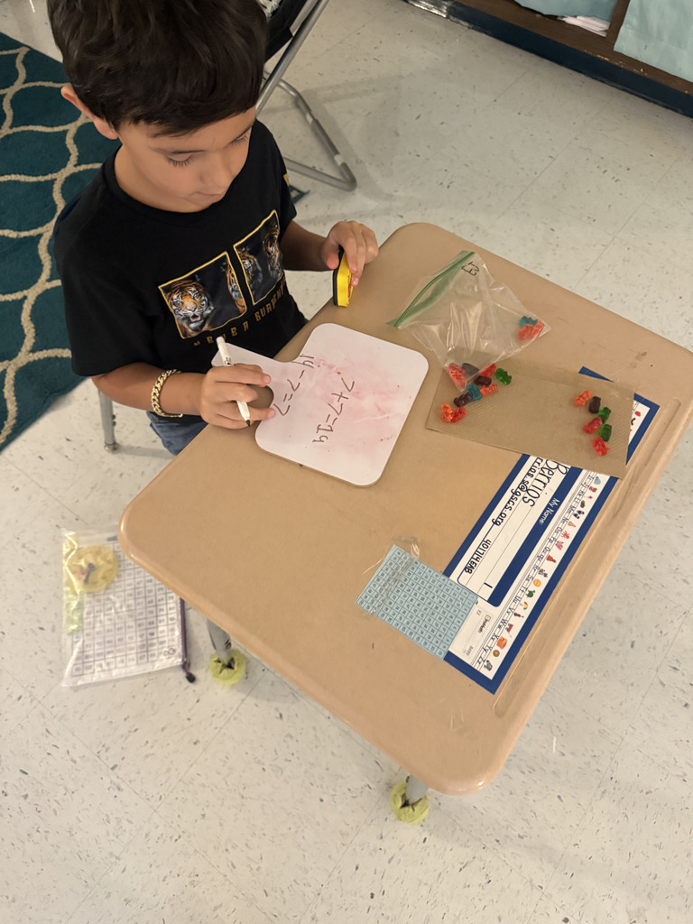 boy at desk with gummy bears, writing math equation
