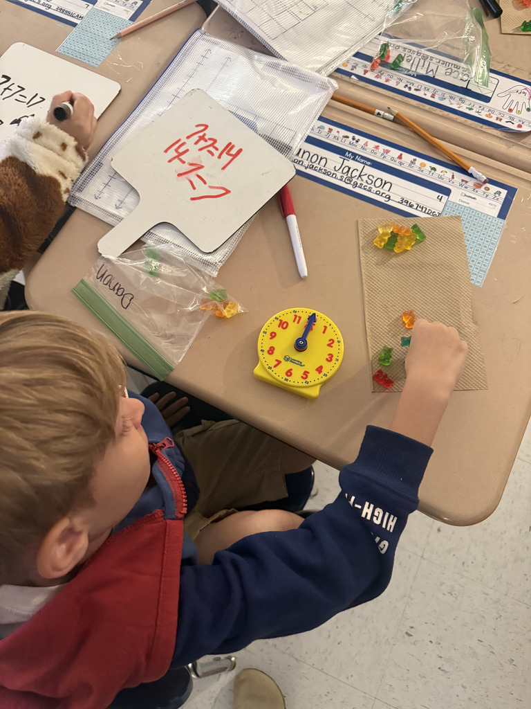 boy at desk with gummy bears, writing math equation