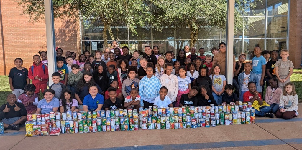 large group of kids in front of large stack of canned food items