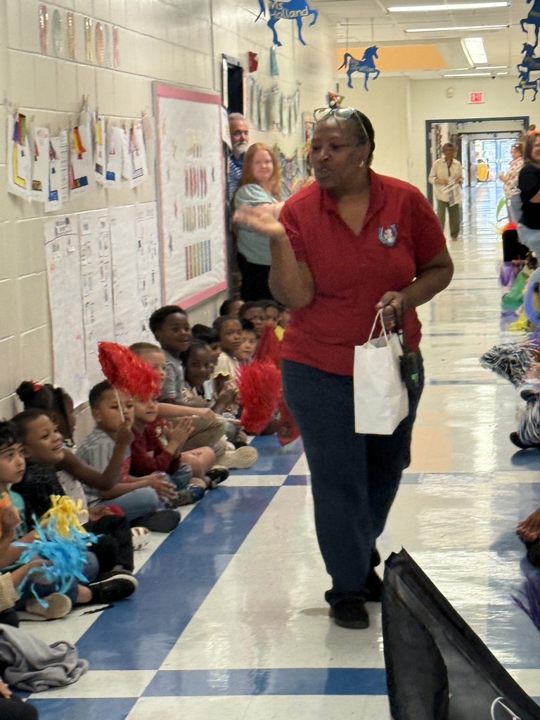 Woman in red polo (blowing a kiss) in middle of hall with students lining walls cheering