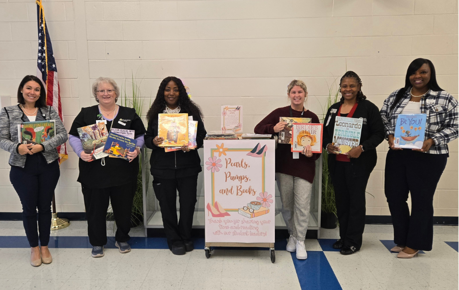 group picture of 6 women holding books in a school hall