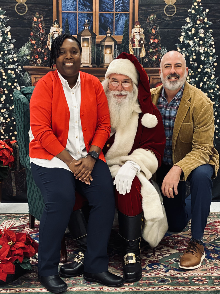 Santa seated in large chair, man kneeling beside, woman on Santa's lap