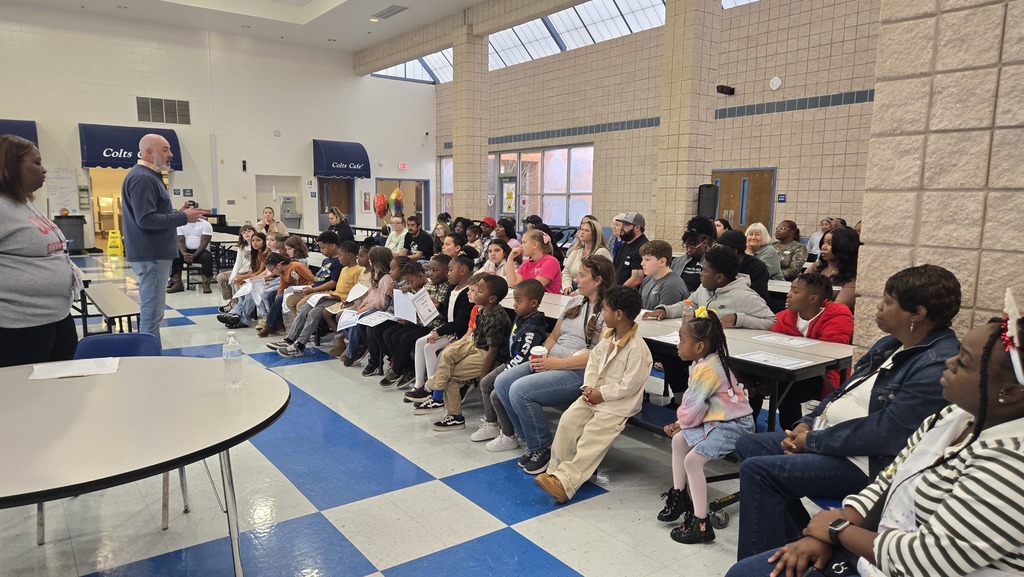 parents and students at tables in cafeteria, 2 adults in front talking