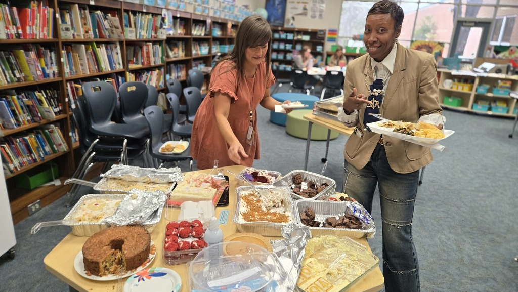 2 women standing at table, filled with desserts