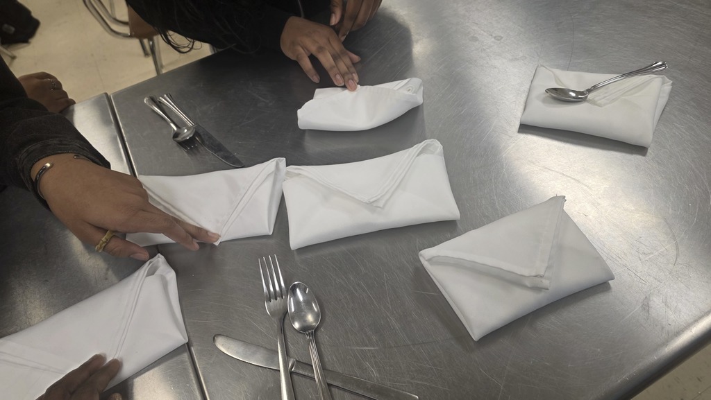 Students practice folding cloth napkins into an "envelope" shape
