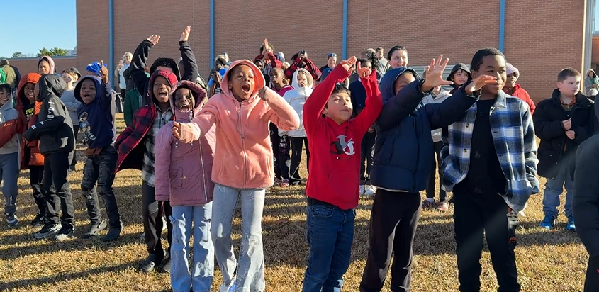 students on hill jumping and waving, excited