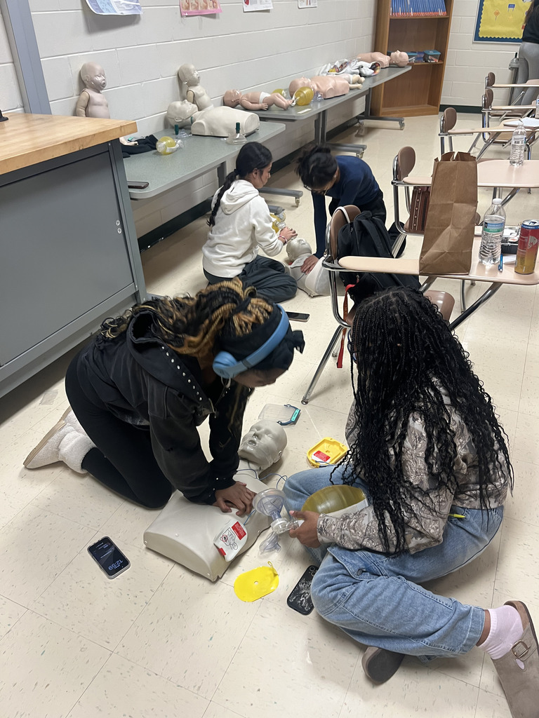 A student performs CPR on a dummy on the floor while another watches