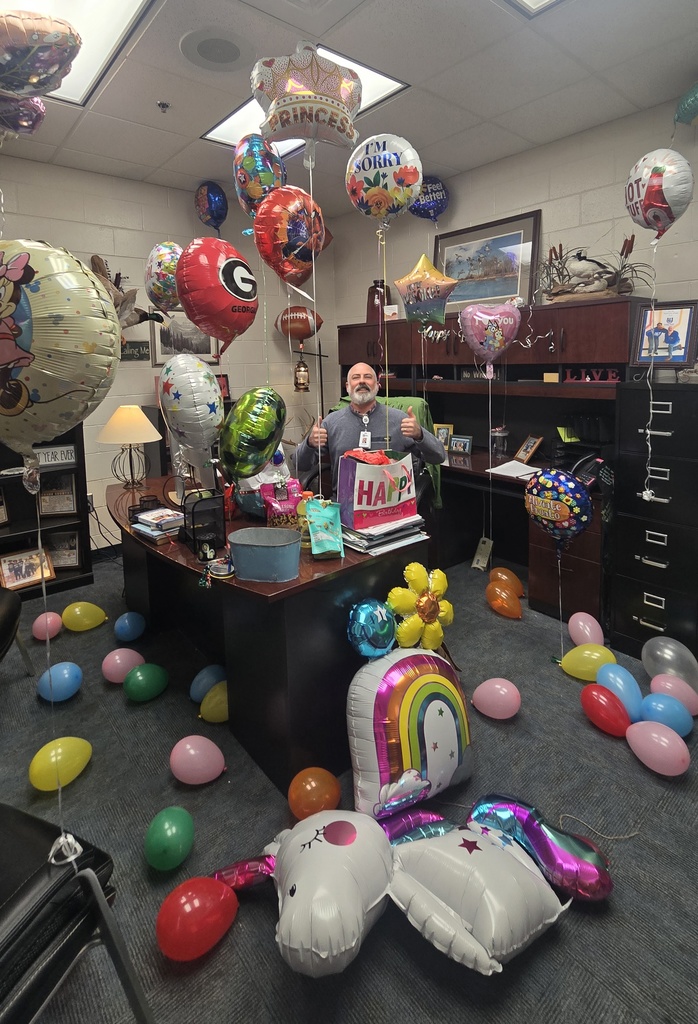 man at desk in office, surrounded by many balloons
