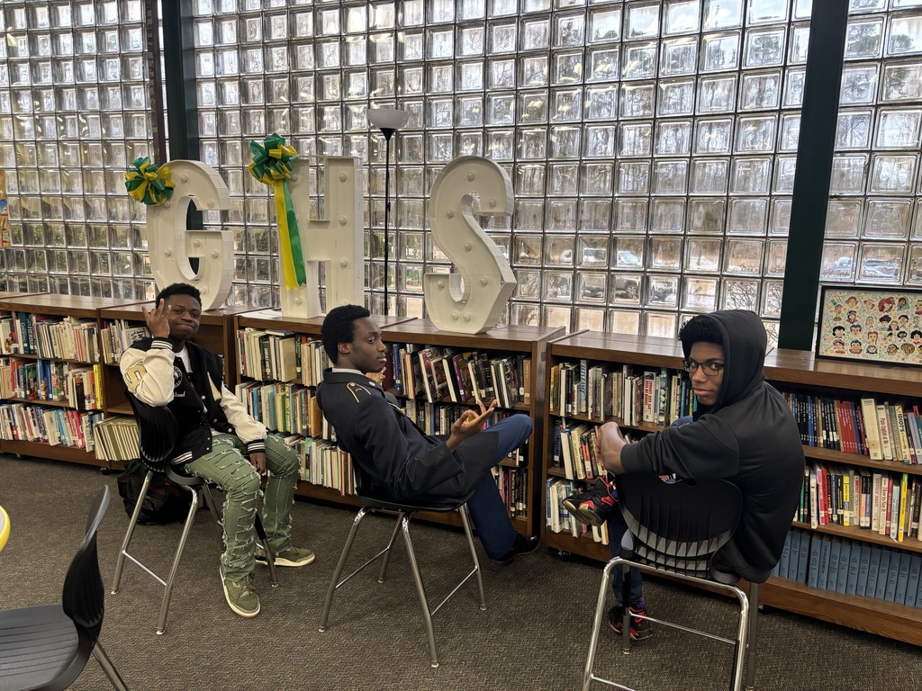 Three students seated in front of bookshelves under a GHS banner