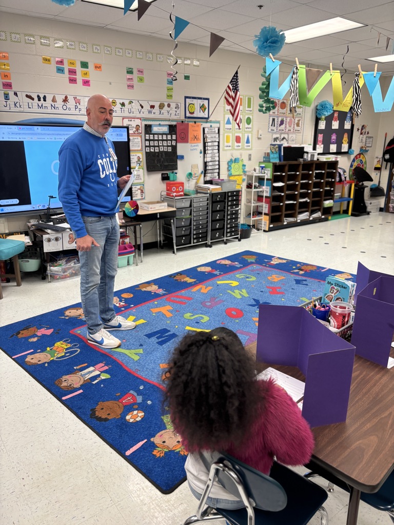 man in front of classroom of Kindergarten students at tables, writing
