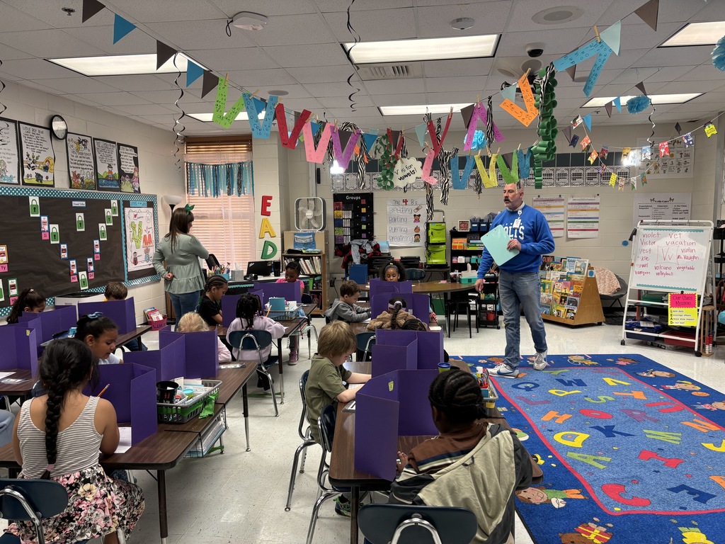 man in front of classroom of Kindergarten students at tables, writing