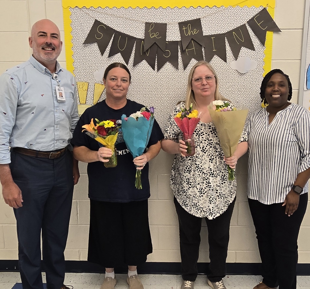 2 ladies holding flowers, a man and a woman on either side of them, in front of a banner reading "Be The sunshine"
