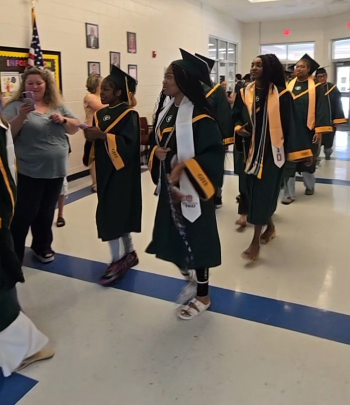 Seniors (in cap and gown) walking in elementary hall