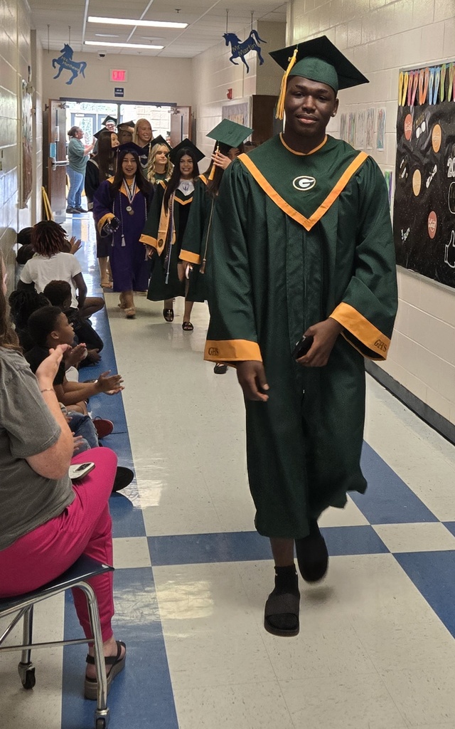Seniors (in cap and gown) walking in elementary hall