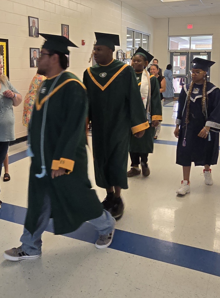 Seniors (in cap and gown) walking in elementary hall